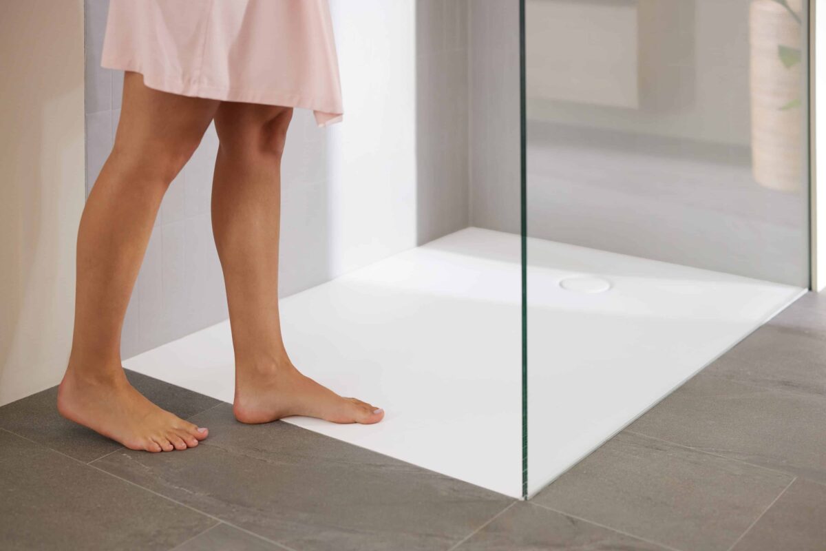 Kobieta wchodzi pod prysznic walk-in ze szklaną ścianką i zlicowanym z podłogą brodzikiem